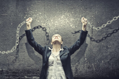 Osoba przełamująca łańcuch na szarym tle – symbol determinacji, siły woli, uwollnieie się od złych nawyków i nowego początku.