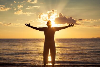 Mężczyzna witający z radością wschód słońca nad morzem - metafora spełnienia
