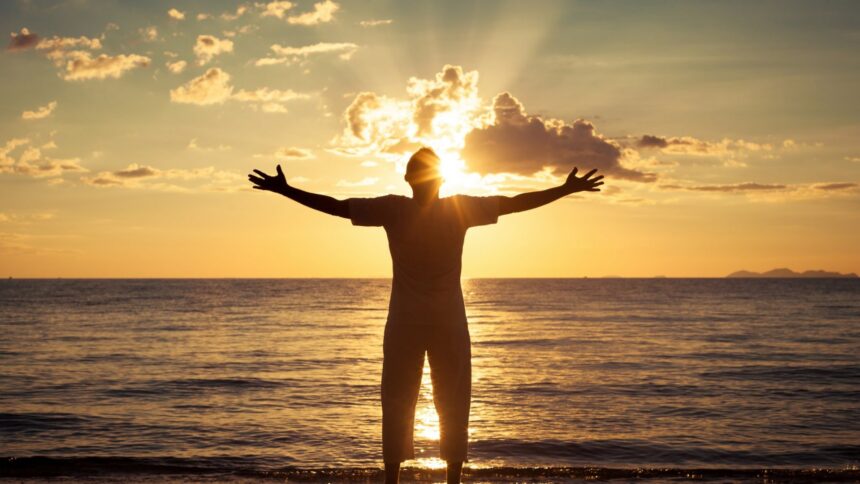 Mężczyzna witający z radością wschód słońca nad morzem - metafora spełnienia