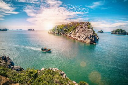 Widok na turkusowe wody i wapienne formacje Zatoki Lan Ha w Wietnamie, z tradycyjną dżonką płynącą między wysepkami.