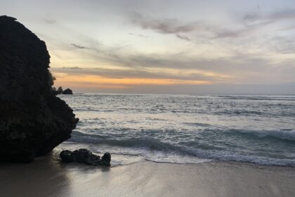 Zachód słońca na plaży w Uluwatu, Bali – fale rozbijające się o brzeg, skaliste klify i pastelowe kolory nieba o zmierzchu.