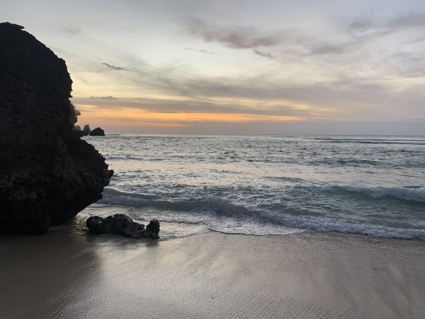 Zachód słońca na plaży w Uluwatu, Bali – fale rozbijające się o brzeg, skaliste klify i pastelowe kolory nieba o zmierzchu.