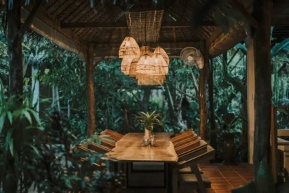 Drewniany stół w otwartej jadalni otoczonej tropikalną roślinnością, oświetlony naturalnymi lampami w stylu boho.