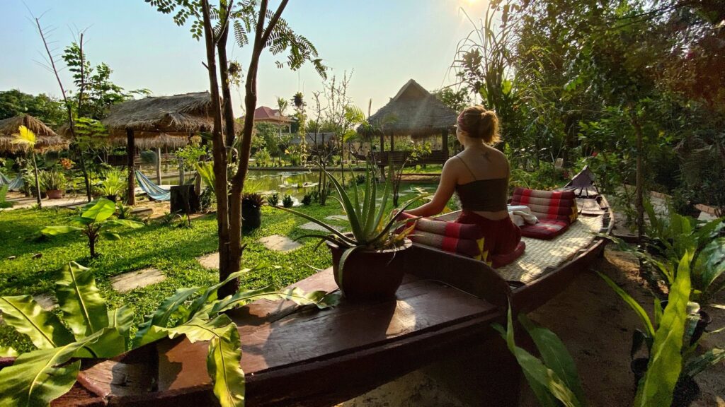 Kobieta medytująca o poranku w ogrodzie Hariharalaya w Kambodży, otoczona zielenią i naturalną ciszą.