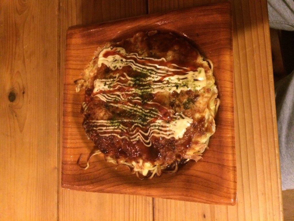 Okonomiyaki – japoński placek z kapustą, sosem i majonezem podany na drewnianej desce.