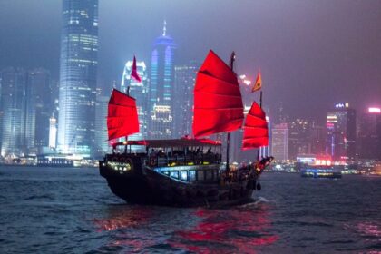 Statek z czerwonymi żaglami na tle nocnej panoramy Hongkongu w Victoria Harbour
