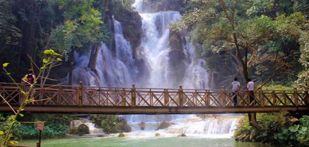 Wodospady Kuang Si w Laosie z drewnianym mostem i turkusową wodą otoczoną tropikalną dżunglą