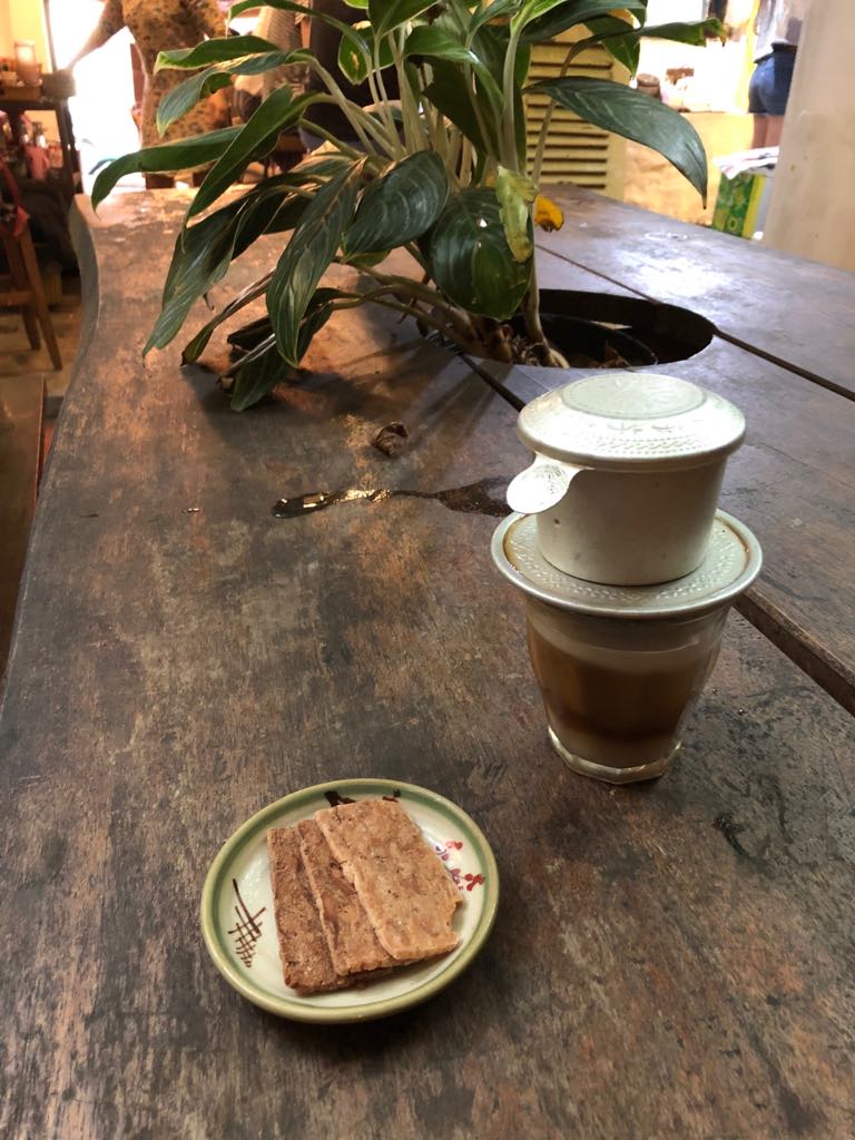 Wietnamska kawa drip i ciasteczko na drewnianym stole w spokojnej kawiarni w Hoi An – chwila ciszy i refleksji