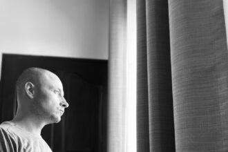A lonely person sitting by a window in a black and white photograph, symbolizing reflection on emotions and the need for authenticity.