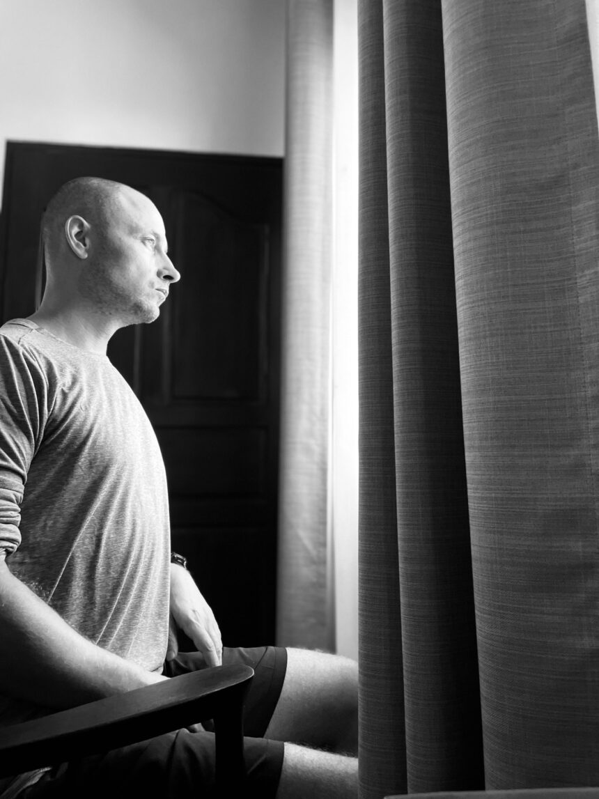 A lonely person sitting by a window in a black and white photograph, symbolizing reflection on emotions and the need for authenticity.